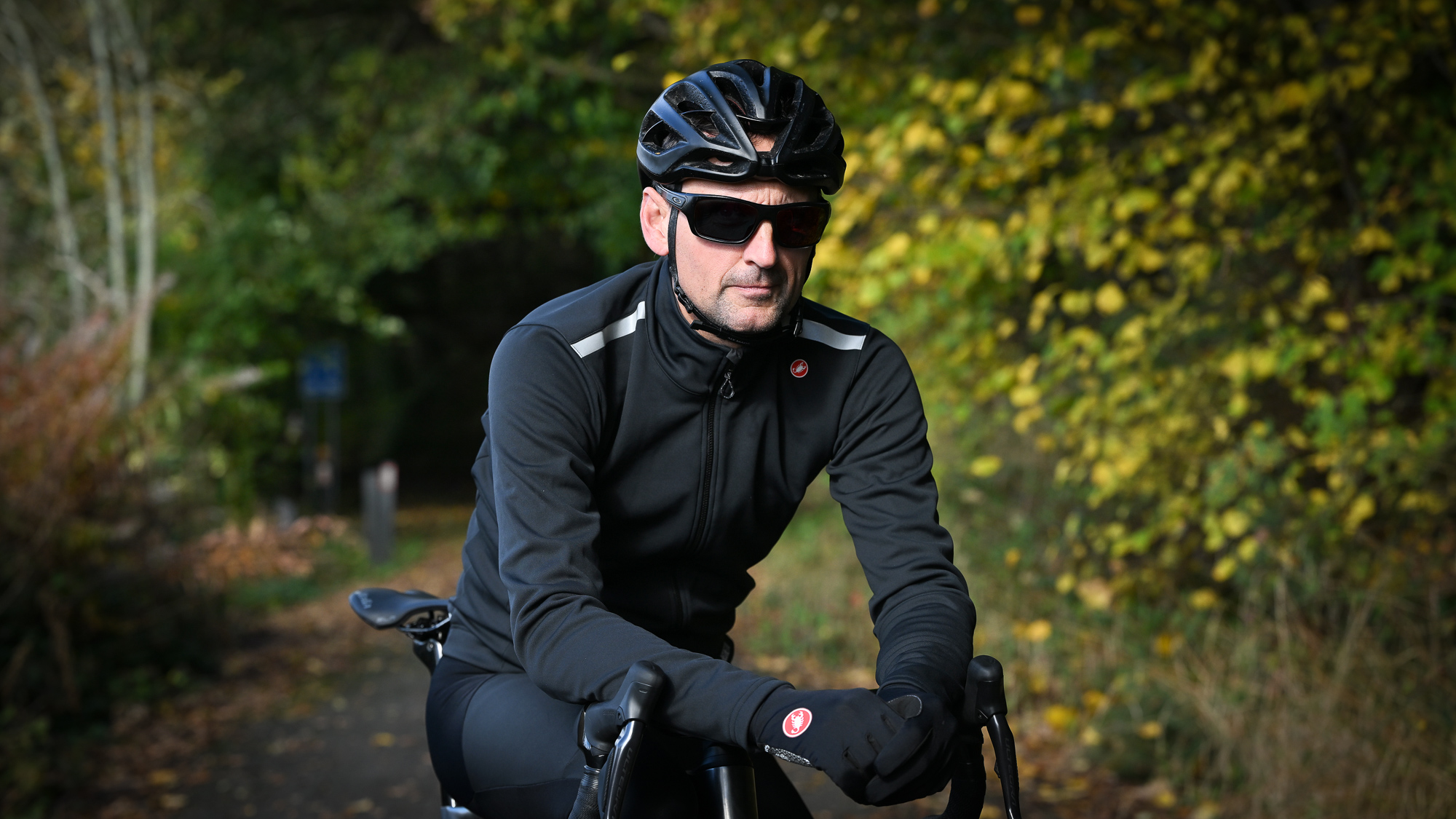 Male rider wearing a black Castelli Espresso Air Jacket on a leafy country lane